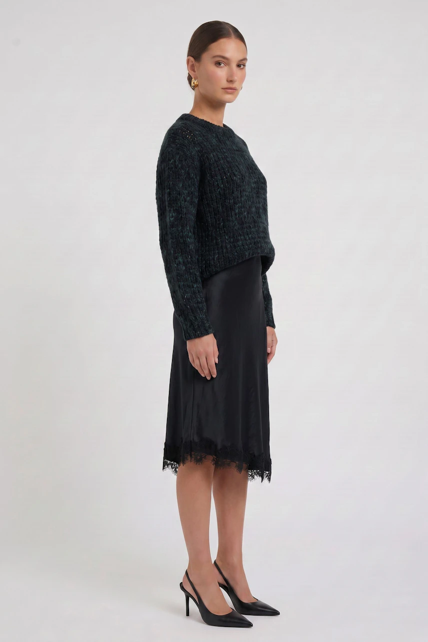 Woman in black pencil skirt with lace hem, paired with a dark textured pullover, standing confidently.