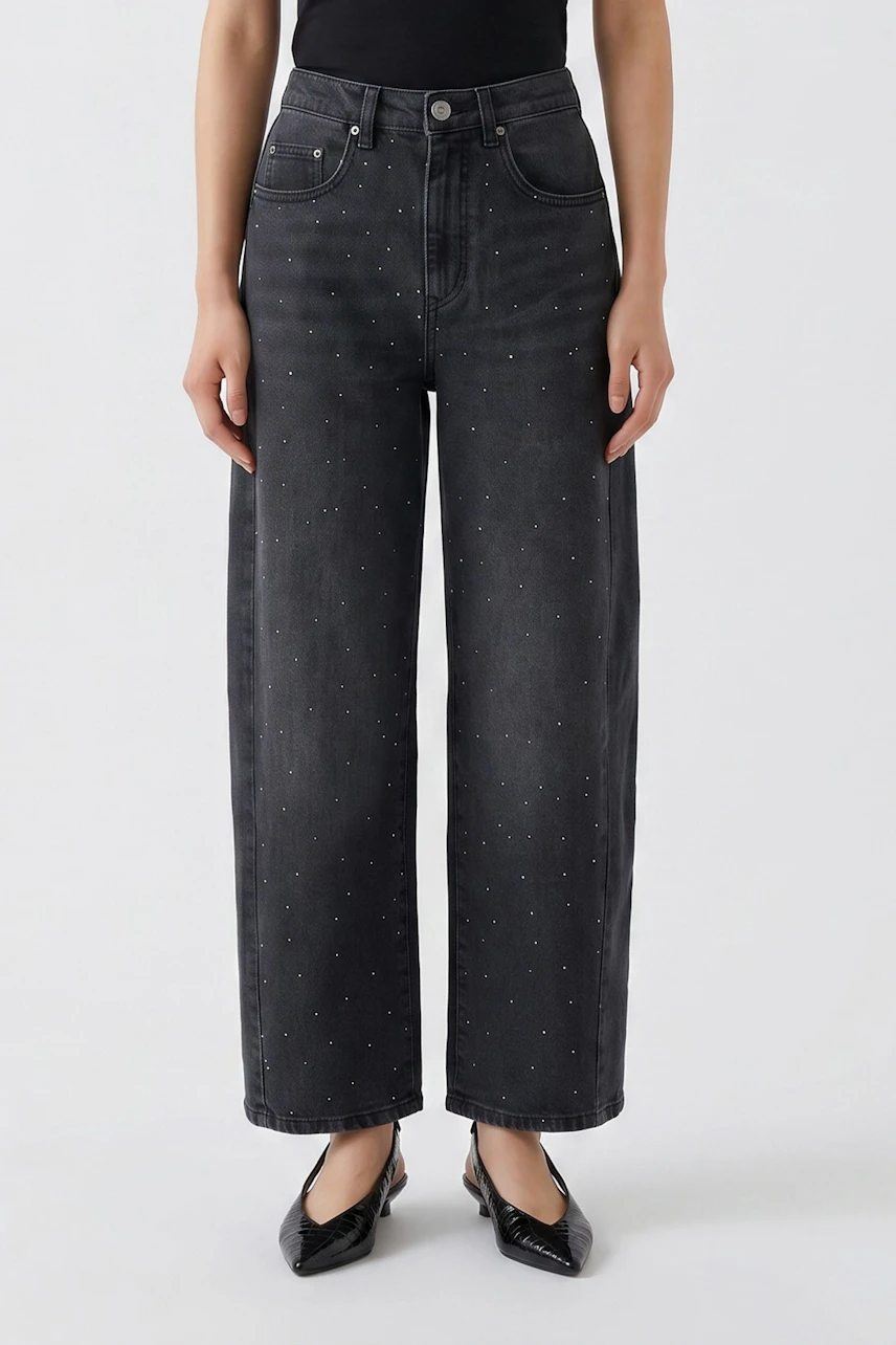 Jeans Barrel: Frau in schwarzer, weiter Jeans mit dezentem Muster und schwarzem Top.
