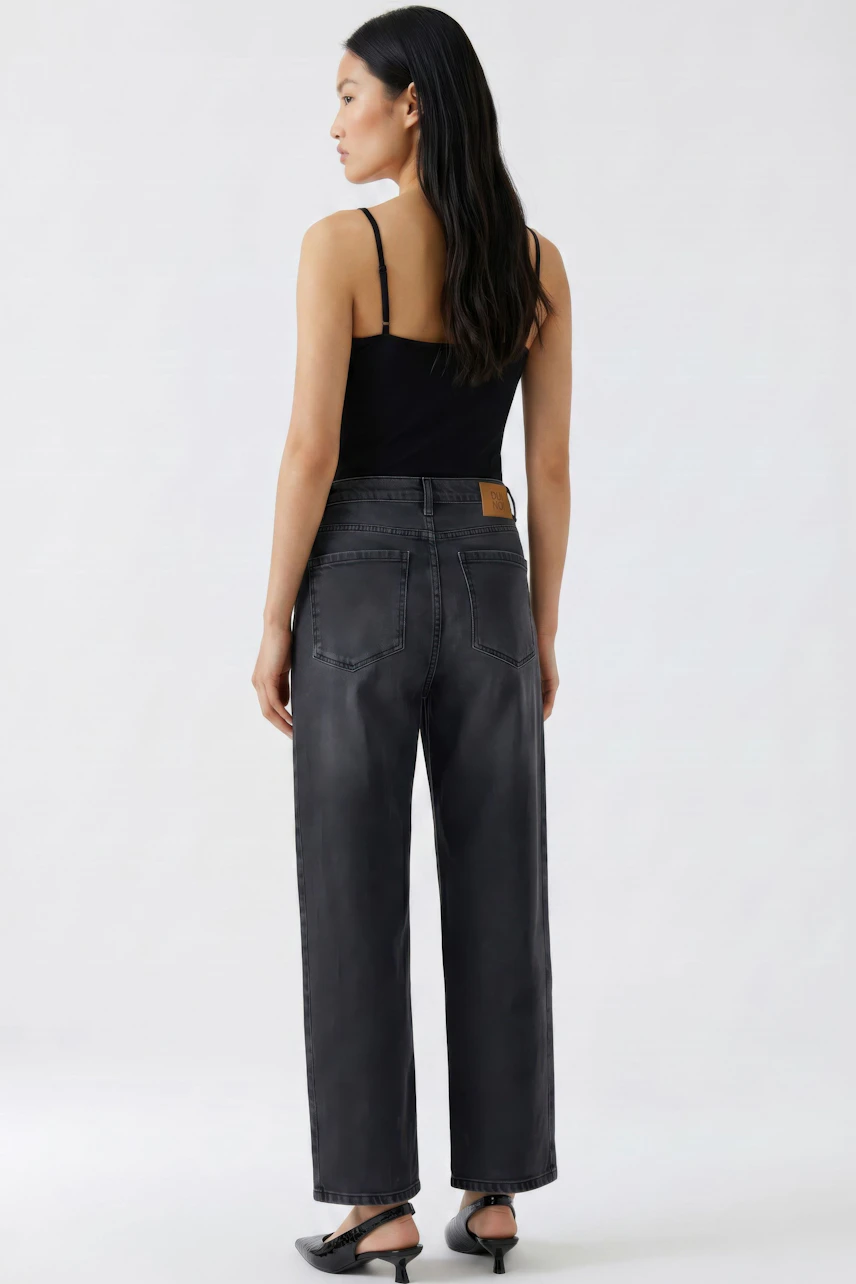 Jeans Barrel: Frau in schwarzem Top und lässiger, dunkler Barrel-Jeans von hinten.