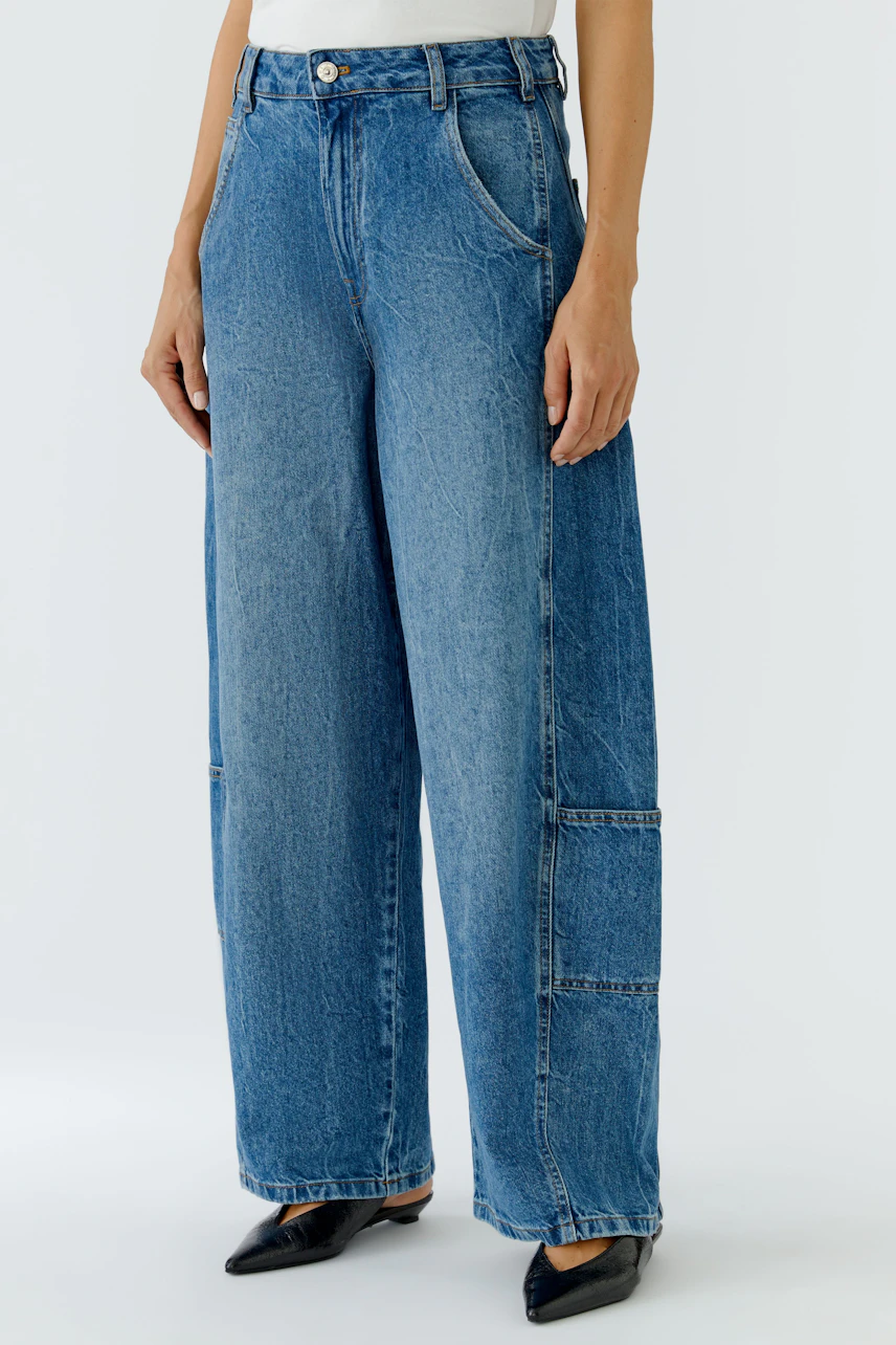 Jeans Barrel: Frau in blauer, weit geschnittener Jeans mit Taschen, kombiniert mit schwarzen Schuhen.