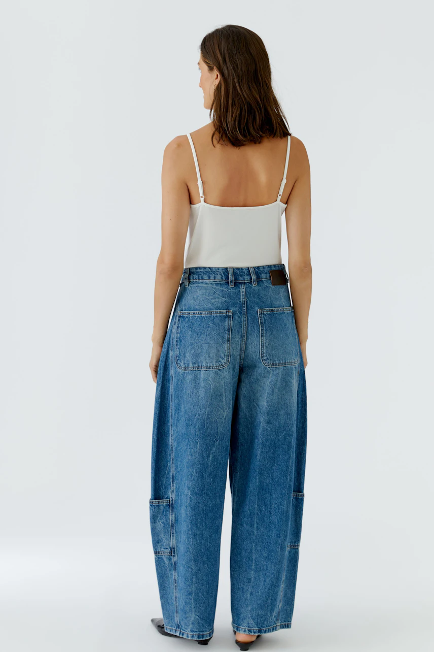 Frau in Jeans Barrel: Lässige, weite Jeans mit großen Taschen, kombiniert mit weißem Top, von hinten gesehen.