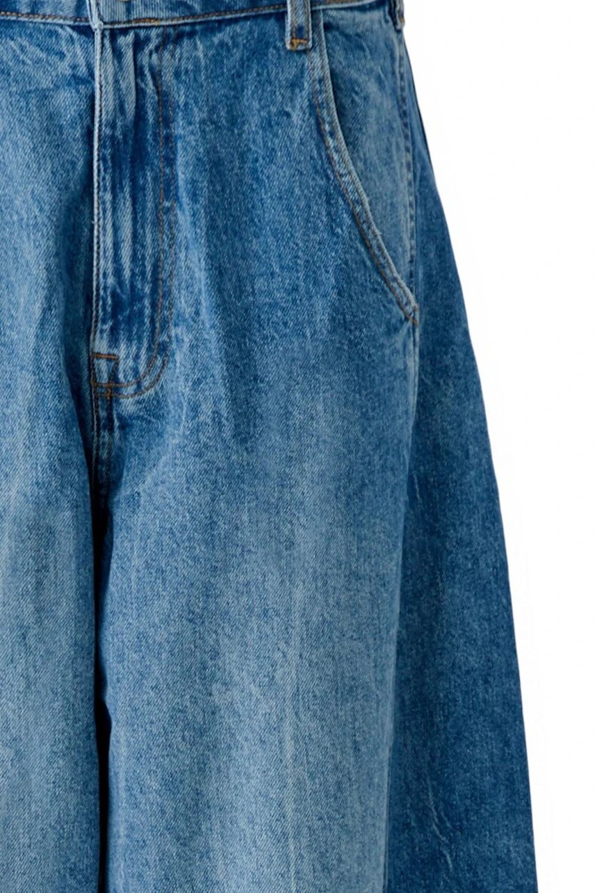 Jeans Barrel: Frau in blauer, weit geschnittener Jeans mit Taschen, kombiniert mit schwarzen Schuhen.