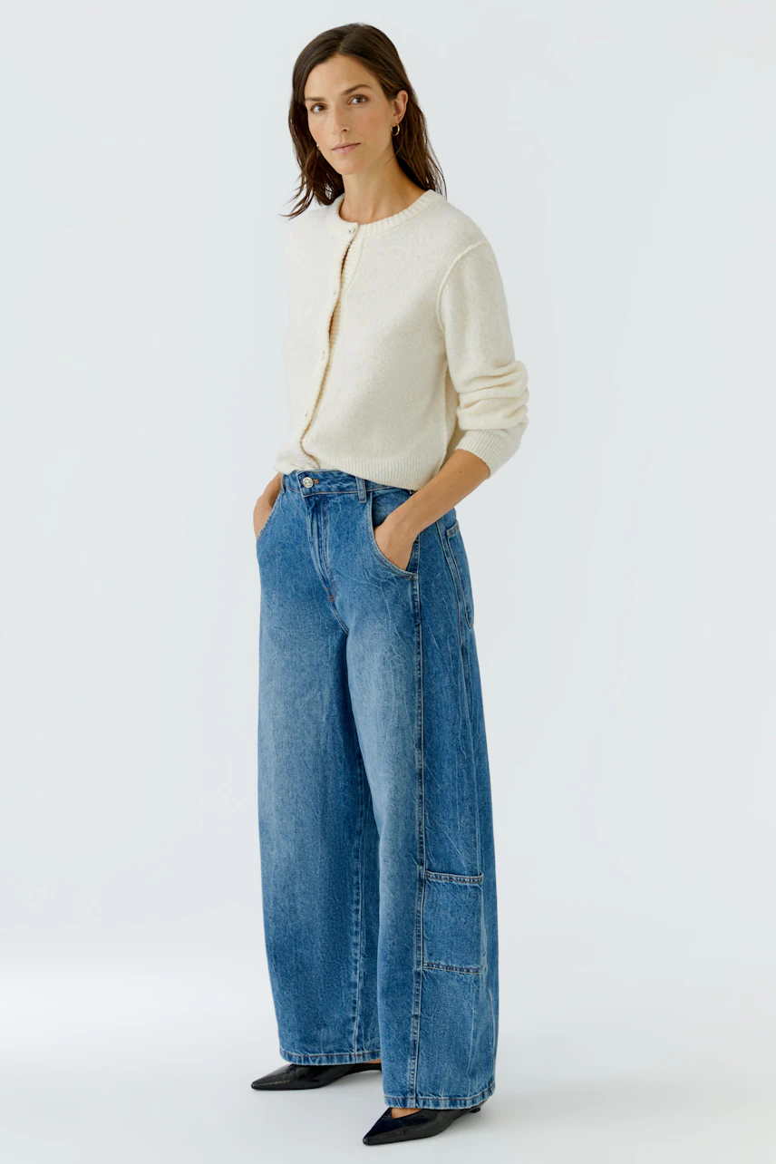 Jeans Barrel: Frau in weiter Jeans und cremefarbenem Cardigan, lässiger Look.