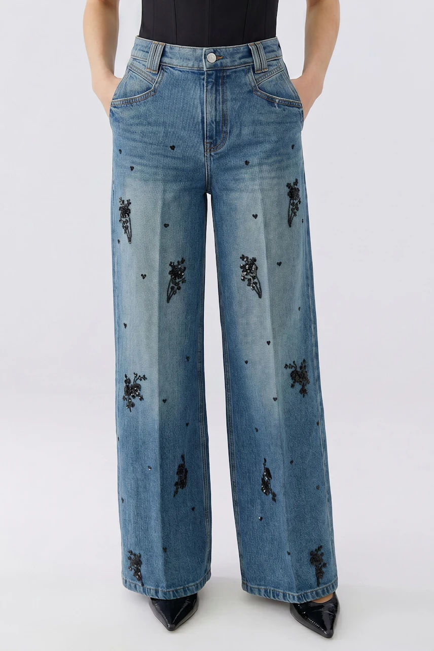 Jeans Wide Leg: Frau in bestickter, weiter Jeans mit schwarzem Top. Lässiger Look für jeden Tag.
