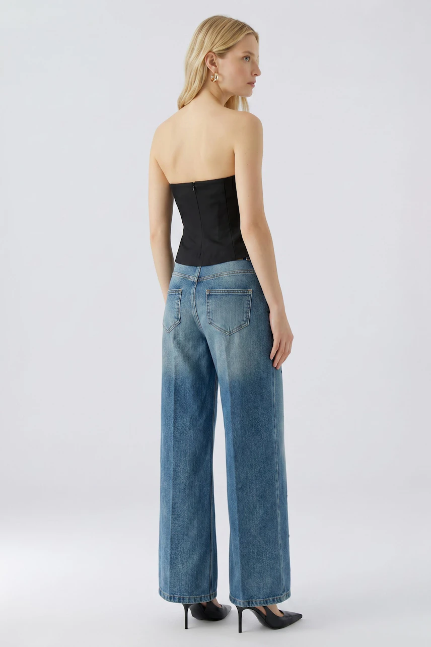 Frau in Jeans Wide Leg: Lässige, weite Jeans mit hohem Bund, kombiniert mit schwarzem Top und Absatzschuhen.