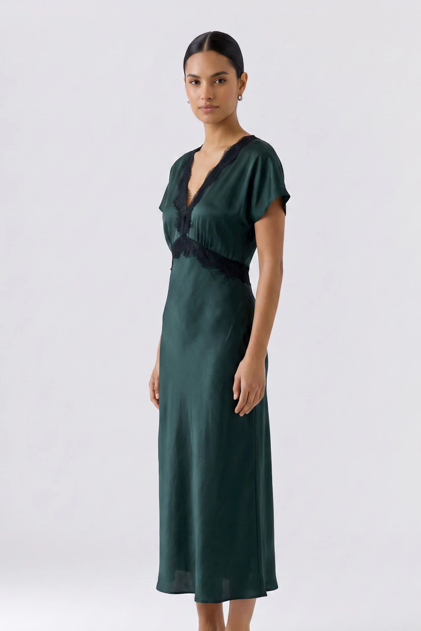 Woman in a sleek green dress with black lace details, standing confidently.