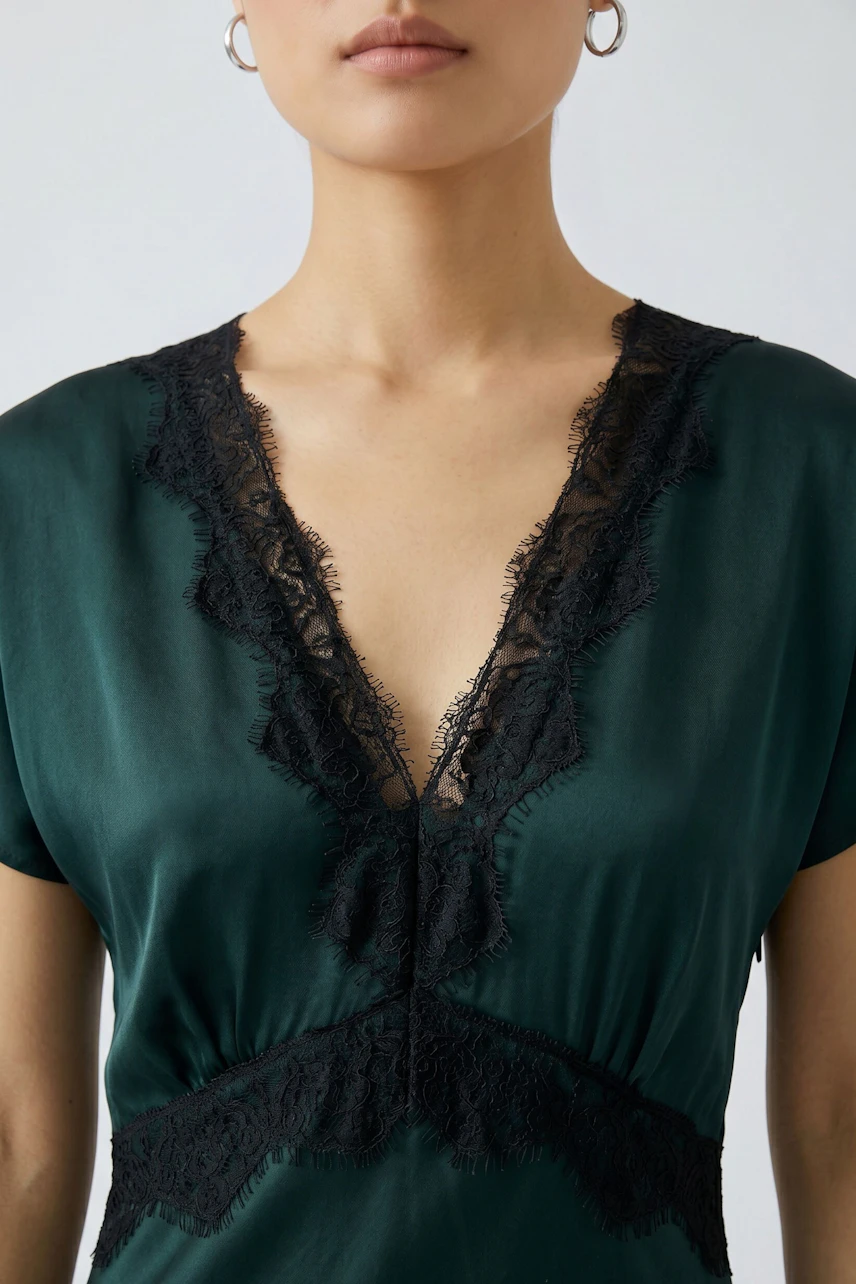 Woman in a green dress with black lace details, showcasing a deep V-neck design.