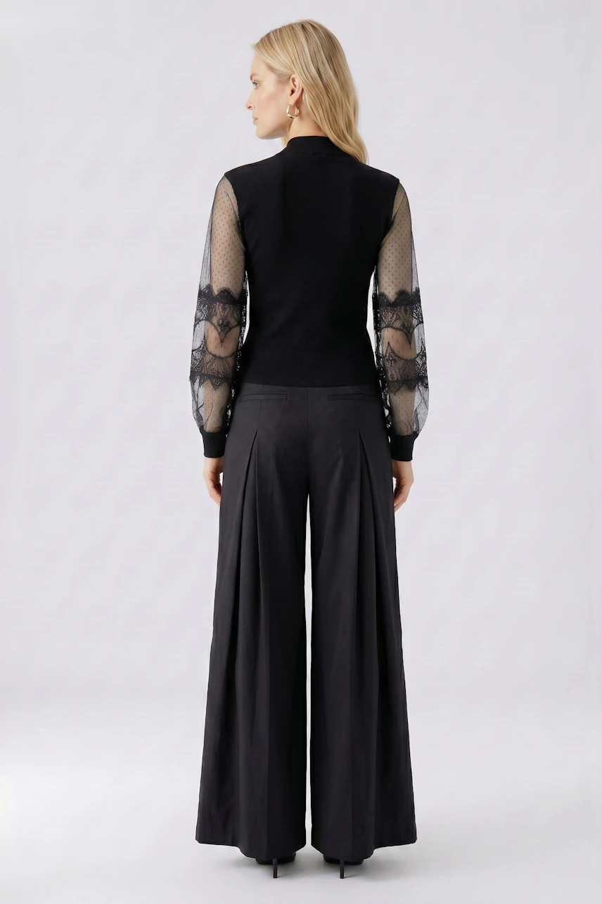 Damen-Pullover: Frau im schwarzen Pullover mit transparenten Ärmeln und weiter Hose von hinten.