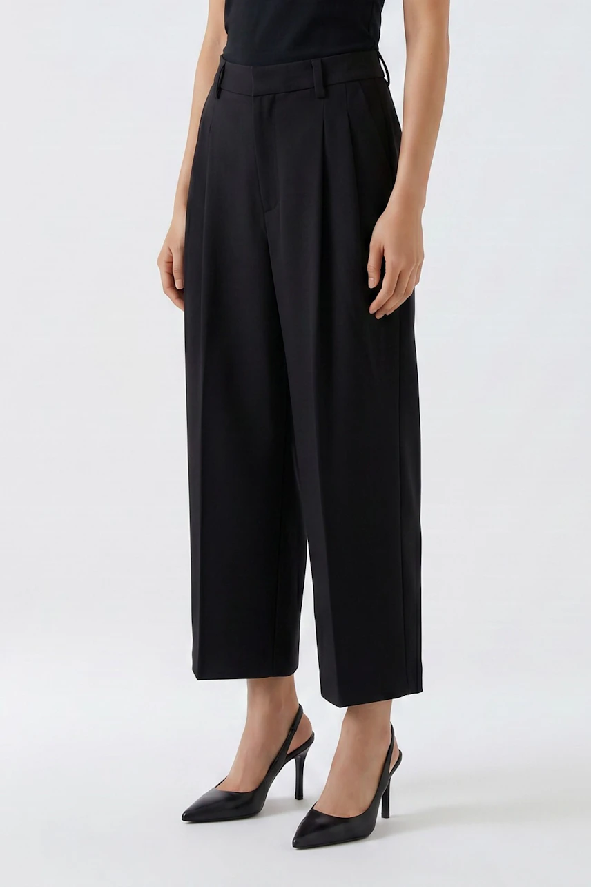 Frau in schwarzer Bundfaltenhose, kombiniert mit schwarzem Top und Pumps. Zeitloser Look für jeden Anlass.