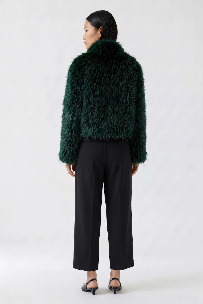 Frau in grüner Kunstfelljacke, schwarze Hose und Sandalen. Die Jacke ist flauschig und modern.