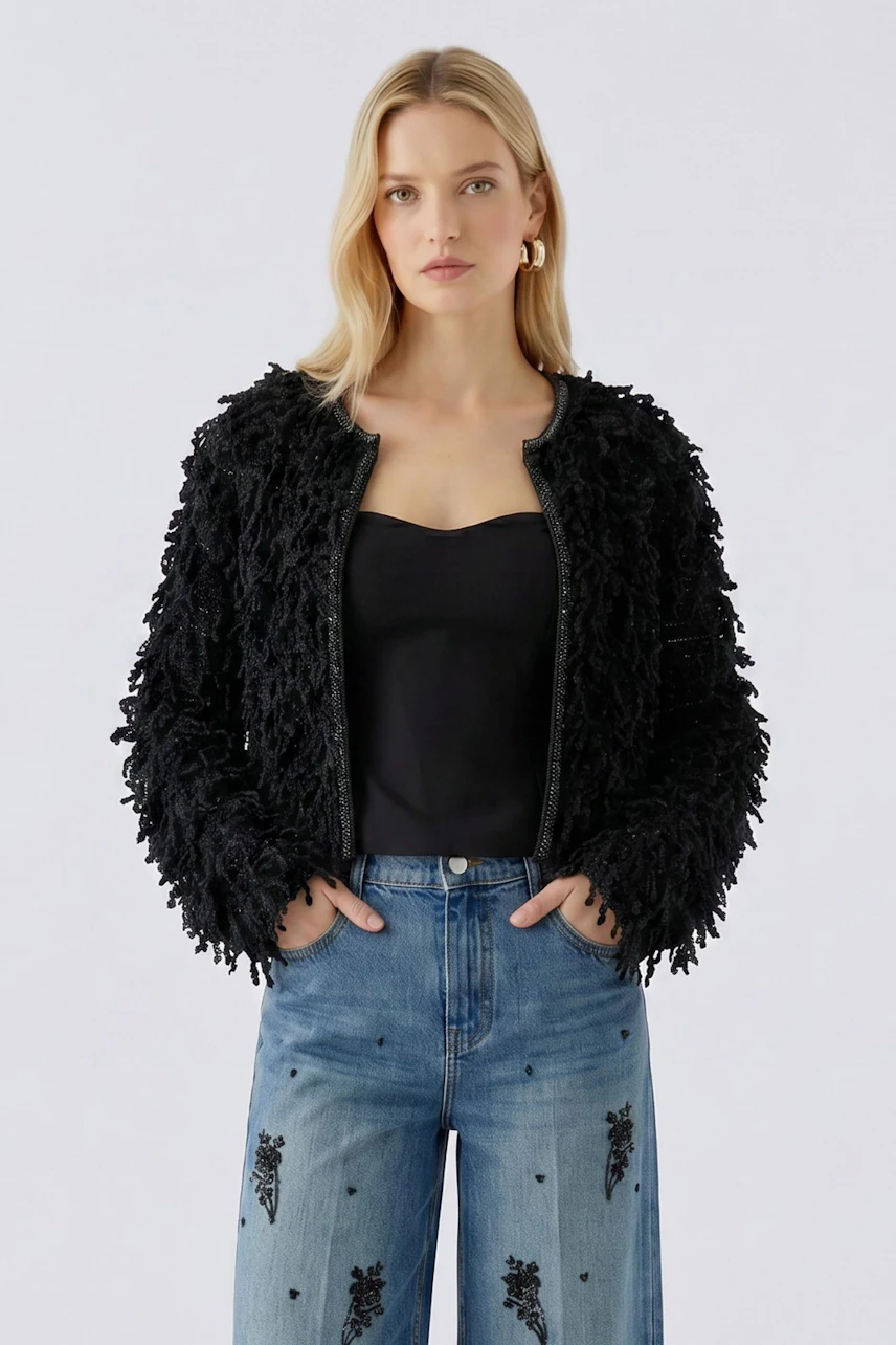 Schwarze Strickjacke: Frau in strukturierter Jacke, schwarzem Top und bestickter Jeans, schaut direkt.