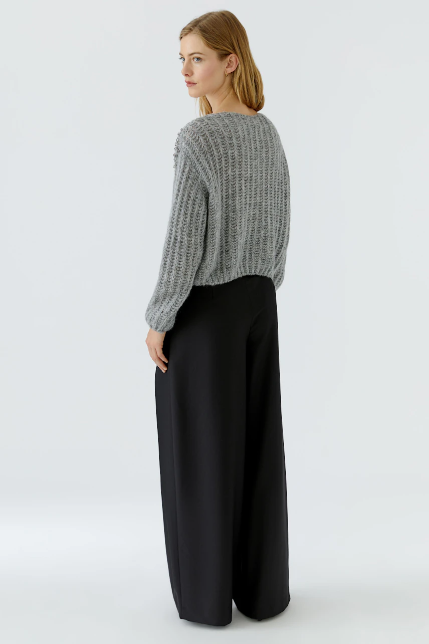 Grauer Damen-Pullover: Frau im lockeren Strickpullover und schwarzen Hosen, seitlich stehend.