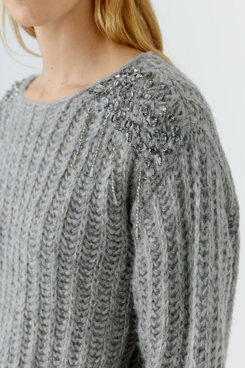Grauer Damen-Pullover: Frau im grob gestrickten Pullover mit funkelnden Details an den Schultern.