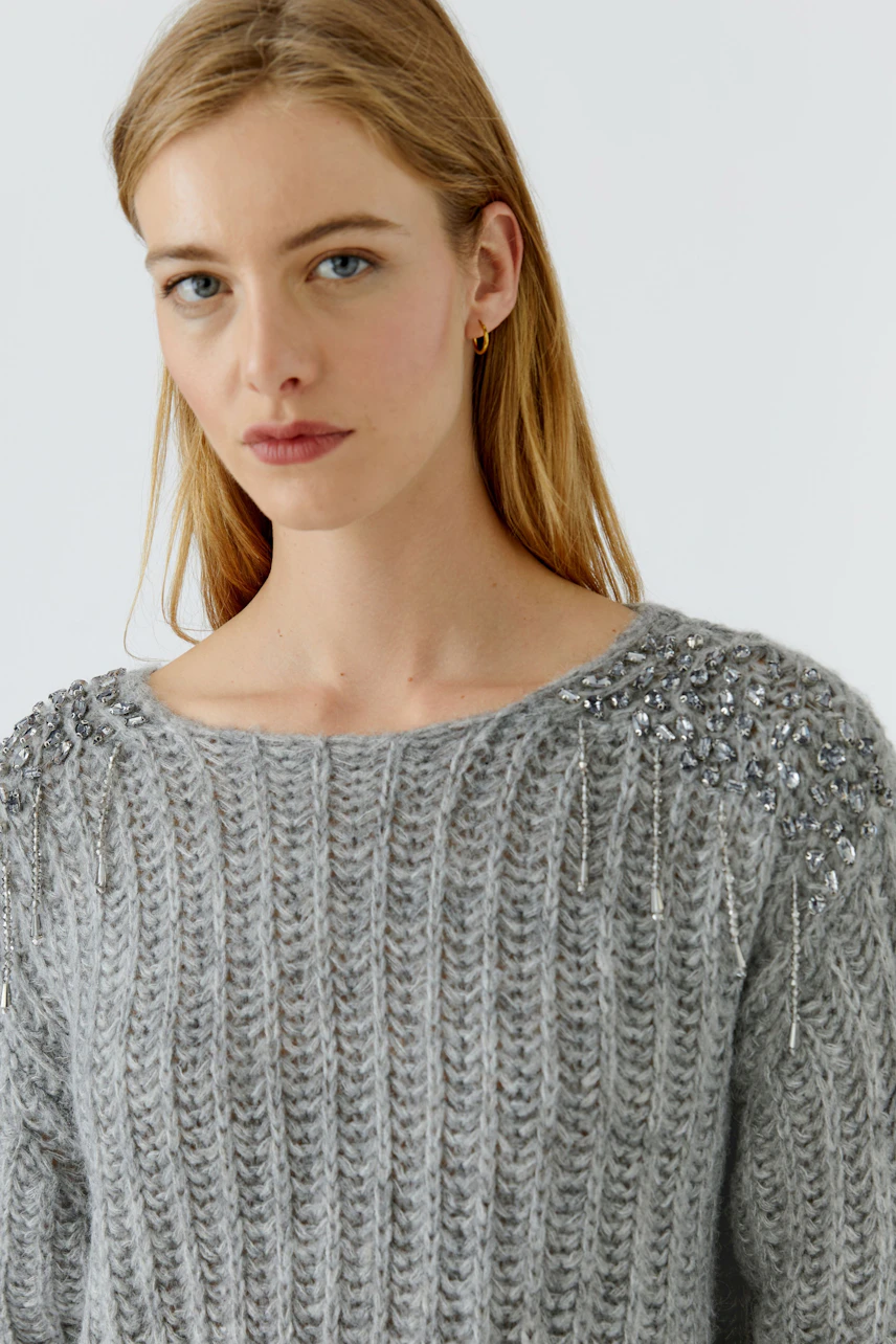 Grauer Damen-Pullover: Frau im grob gestrickten Pullover mit funkelnden Details an den Schultern.