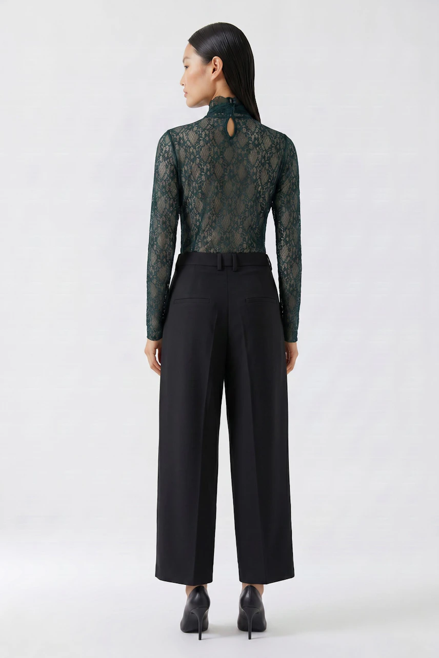Woman in a lace long-sleeve shirt, paired with black wide-leg pants, standing confidently.