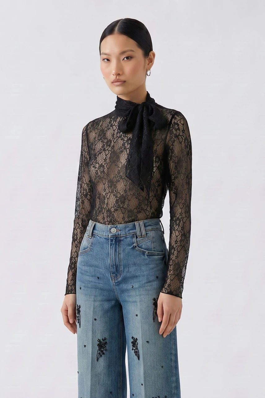Woman in lace long-sleeve shirt with scarf, paired with embroidered jeans, standing confidently.