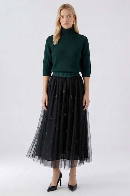 Black A-line skirt with sheer overlay and plaid waistband, displayed on a hanger.