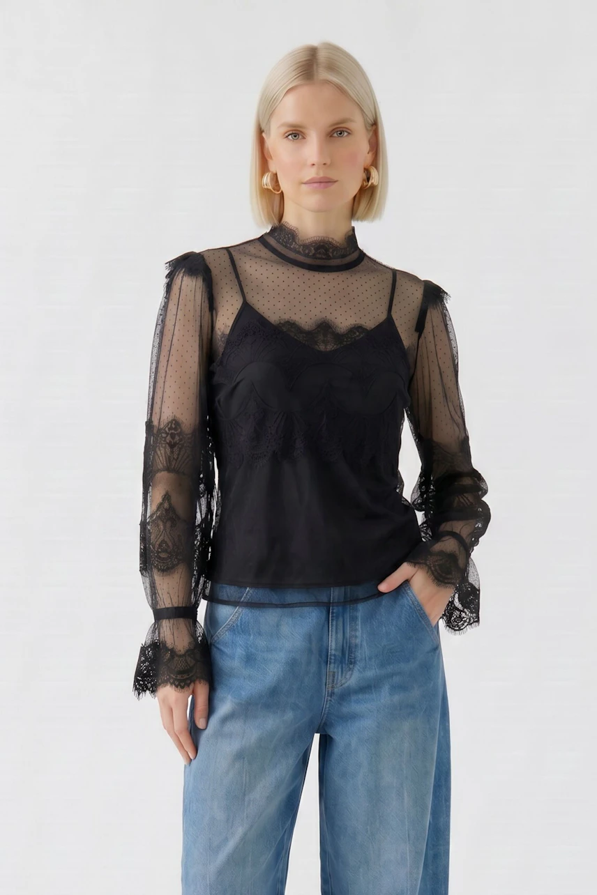 Schwarze Bluse: Frau in transparenter Spitzenbluse mit langen Ärmeln und blauer Jeans.