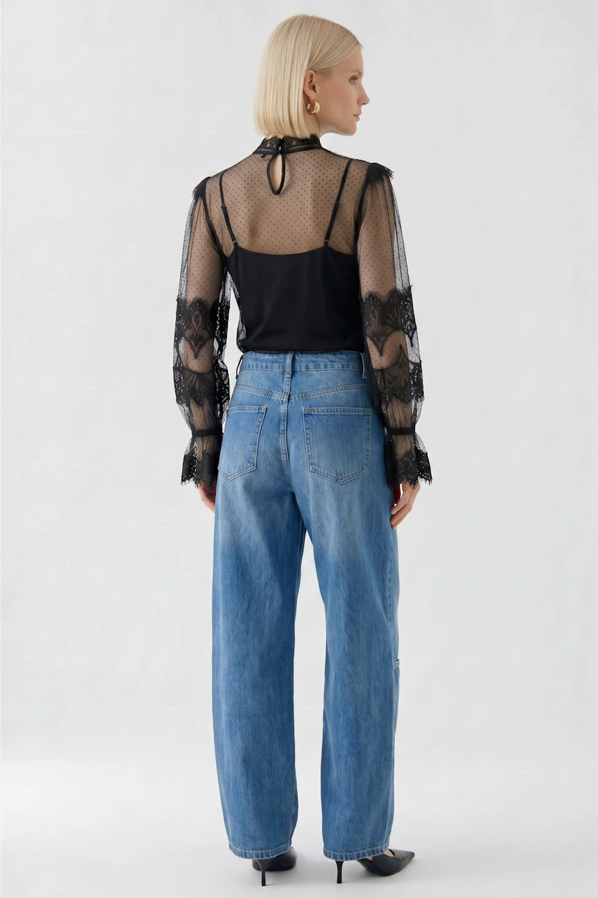 Schwarze Bluse: Frau in transparenter Spitzenbluse mit Jeans, Rückansicht. Modisch und vielseitig kombinierbar.