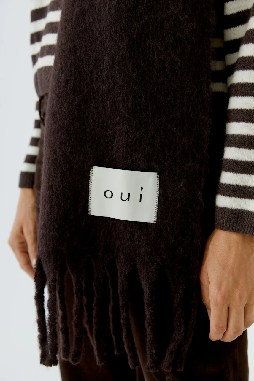 Striped sweater: Woman in a cozy striped sweater with a dark scarf featuring 'oui' logo.