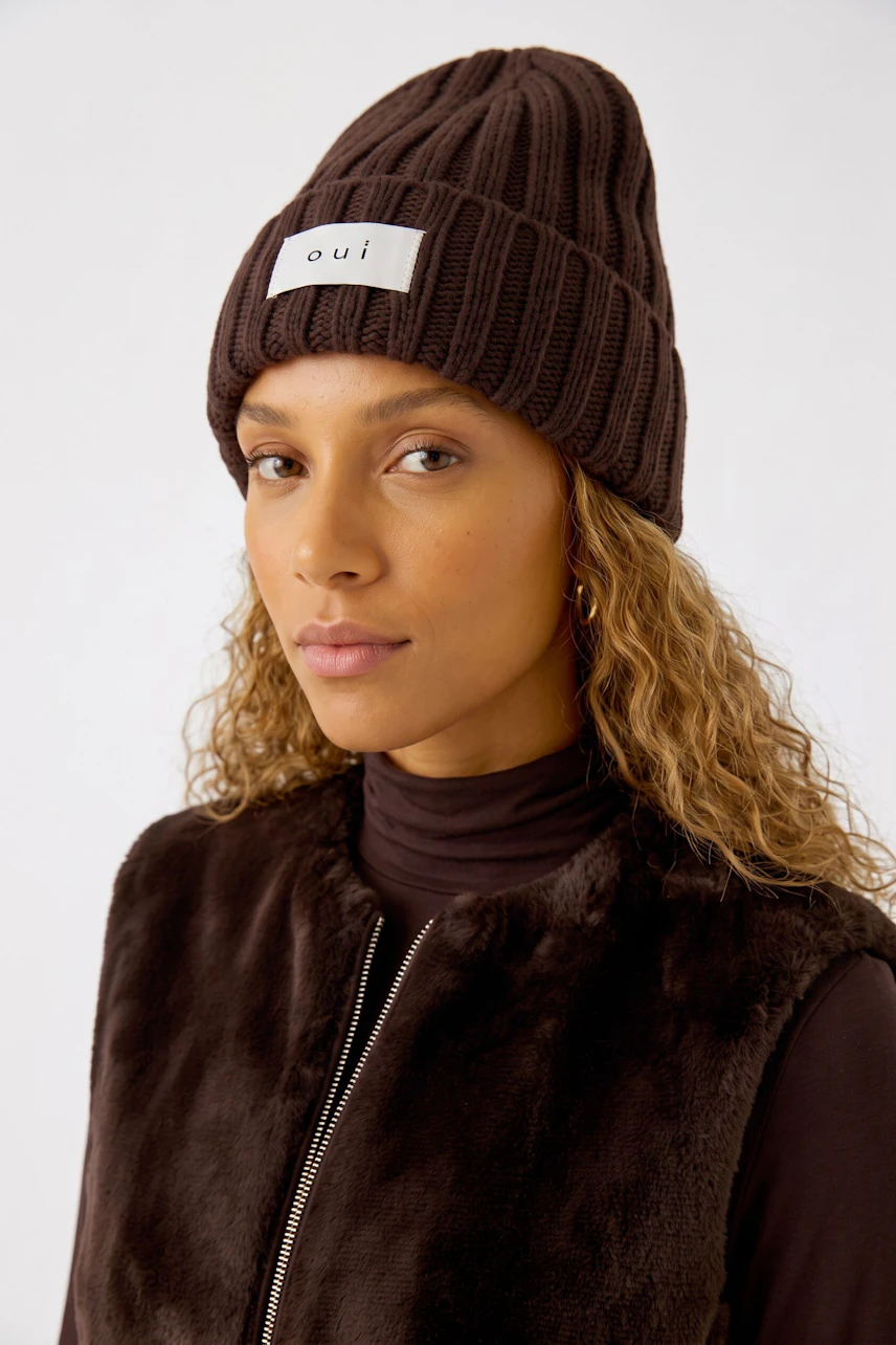 Damen-Mütze: Frau mit brauner Strickmütze und Fellweste, lässiger Look.