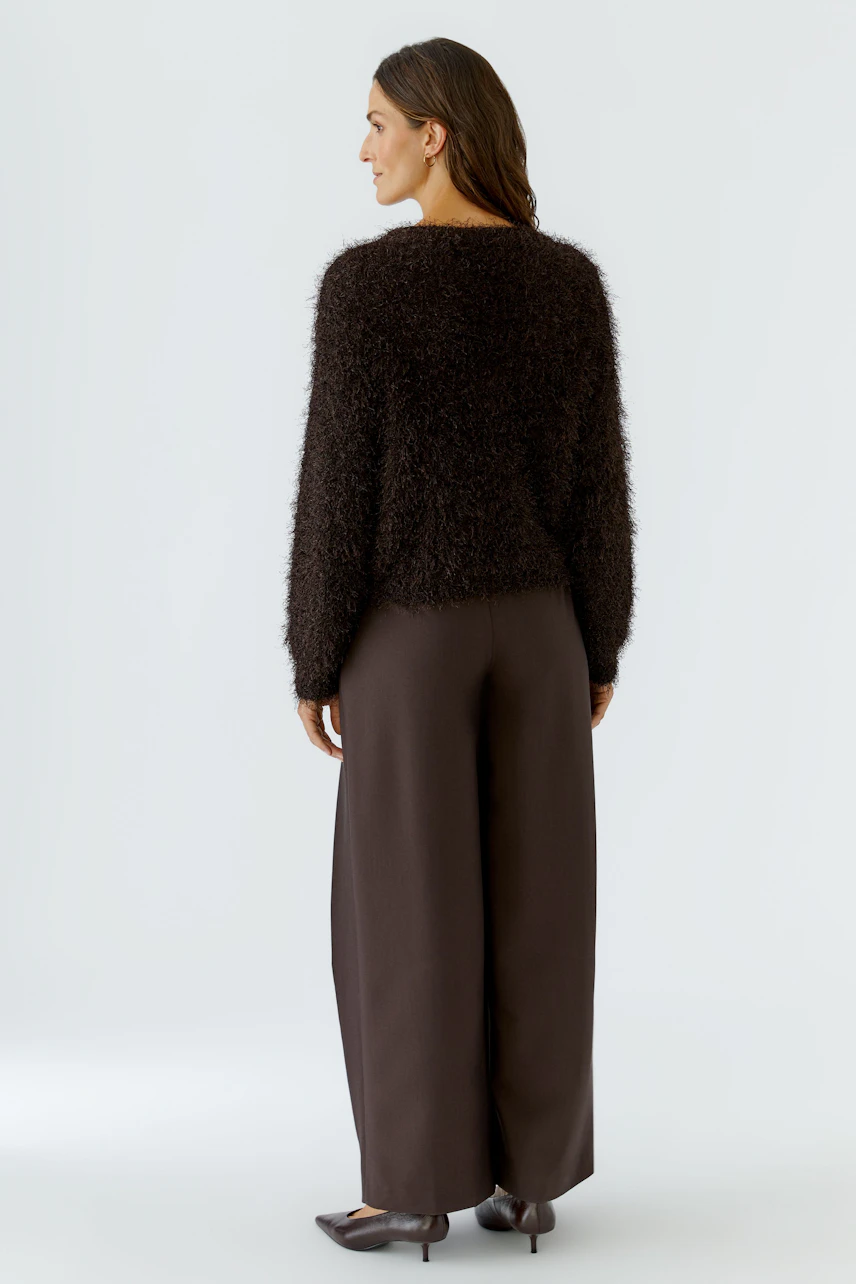 Frau im flauschigen, braunen Pullover, kombiniert mit weiter Hose. Rückansicht des lässigen Looks.