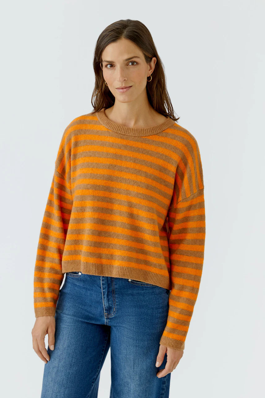 Lässiger Damen-Pullover: Frau im orange-gestreiften Pullover und Jeans, entspannt und modisch.