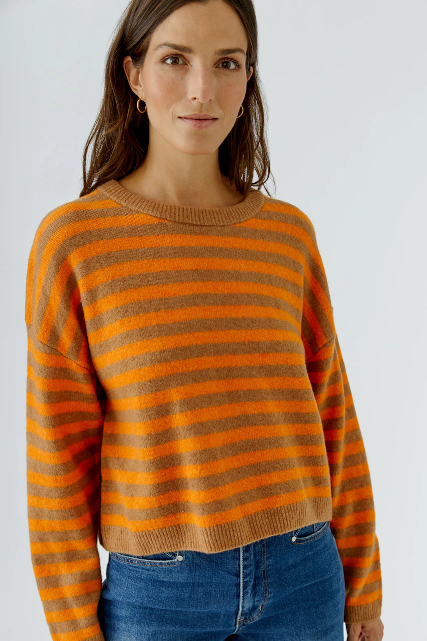 Gestreifter Damen-Pullover: Frau im orange-braunen Pullover mit Rundhalsausschnitt und blauen Jeans.