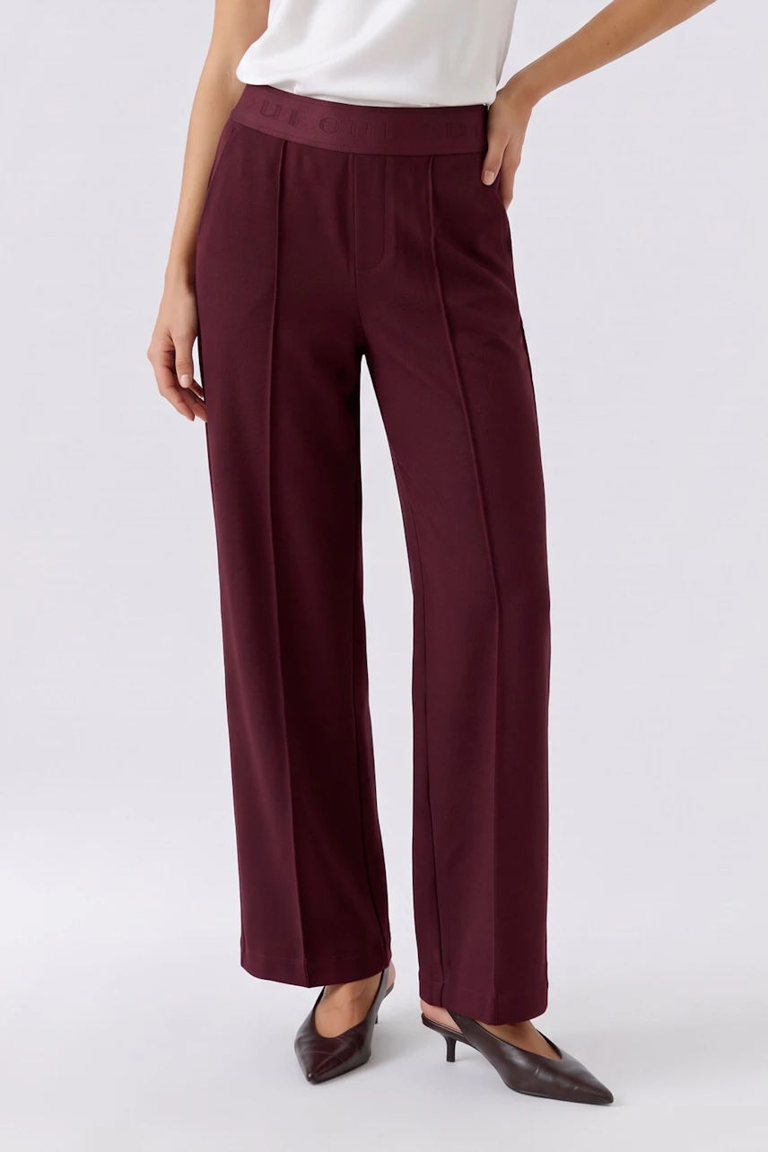 Woman in burgundy pants, white top, and brown heels. The pants have a high waist and straight leg design.
