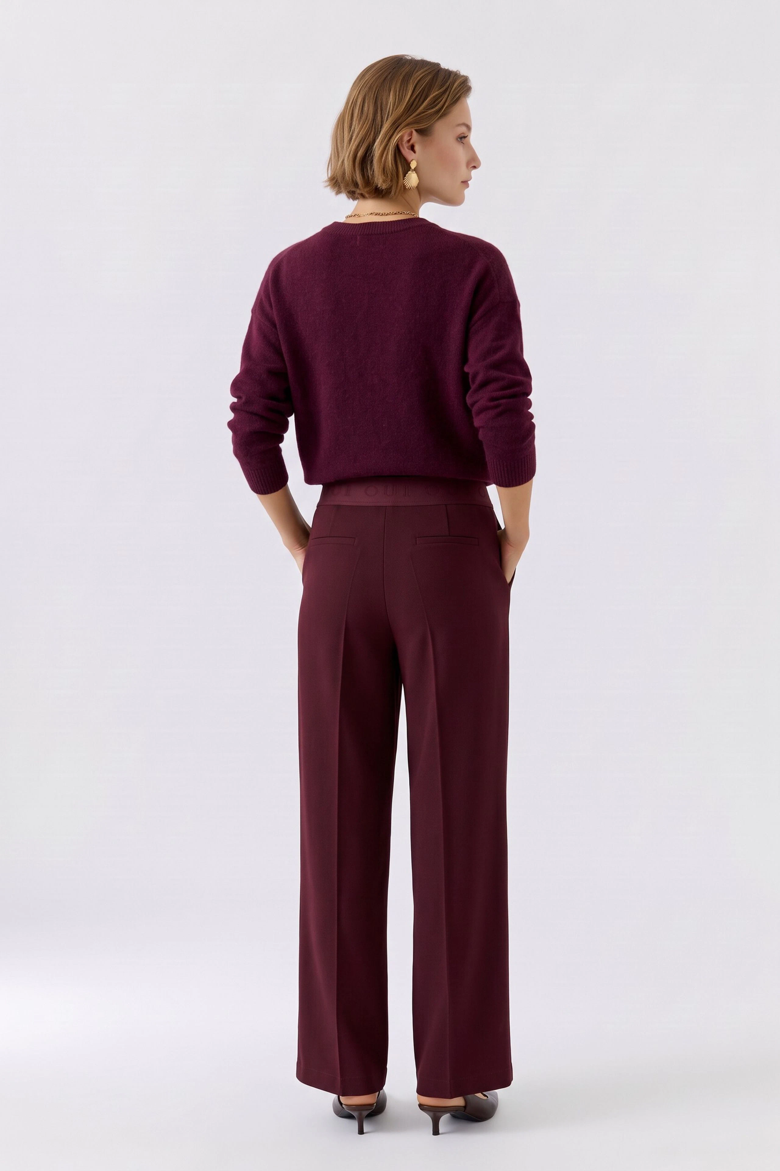 Frau in bordeauxfarbener Hose und passendem Pullover, von hinten gesehen. Lässiger Look für den Alltag.