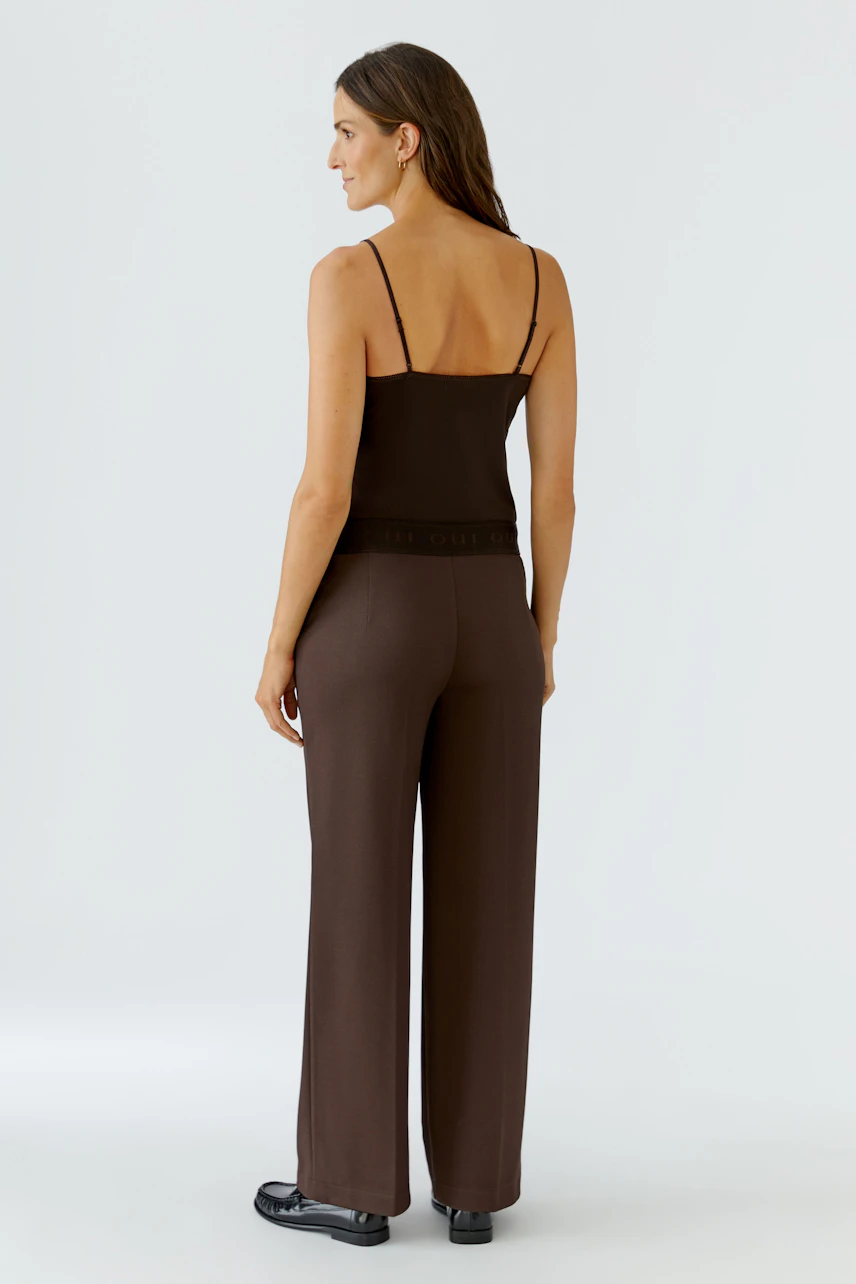 Braune Damen-Hose: Frau in weiter Hose und Top, von hinten, mit schwarzen Schuhen.