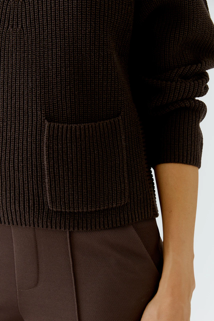 Brauner Damen-Pullover: Frau trägt lässigen Strickpullover mit Tasche, kombiniert mit passender Hose.