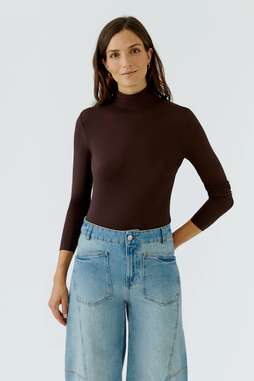 Langarmshirt: Frau im braunen Langarmshirt mit Rollkragen und blauer Jeans, lässig und modern.
