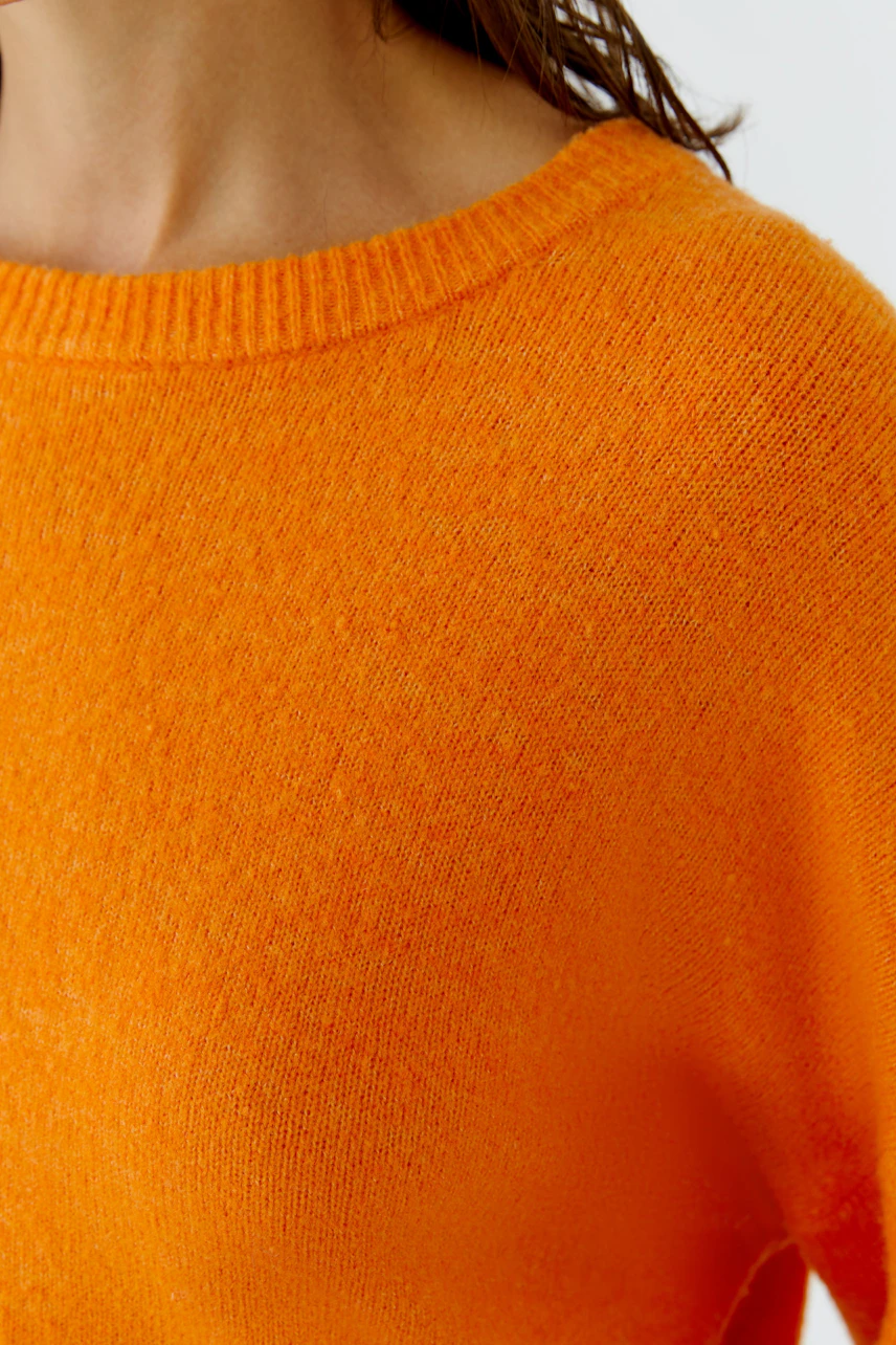 Frau im leuchtend orangefarbenen Pullover mit Rundhalsausschnitt, lässig und modern.