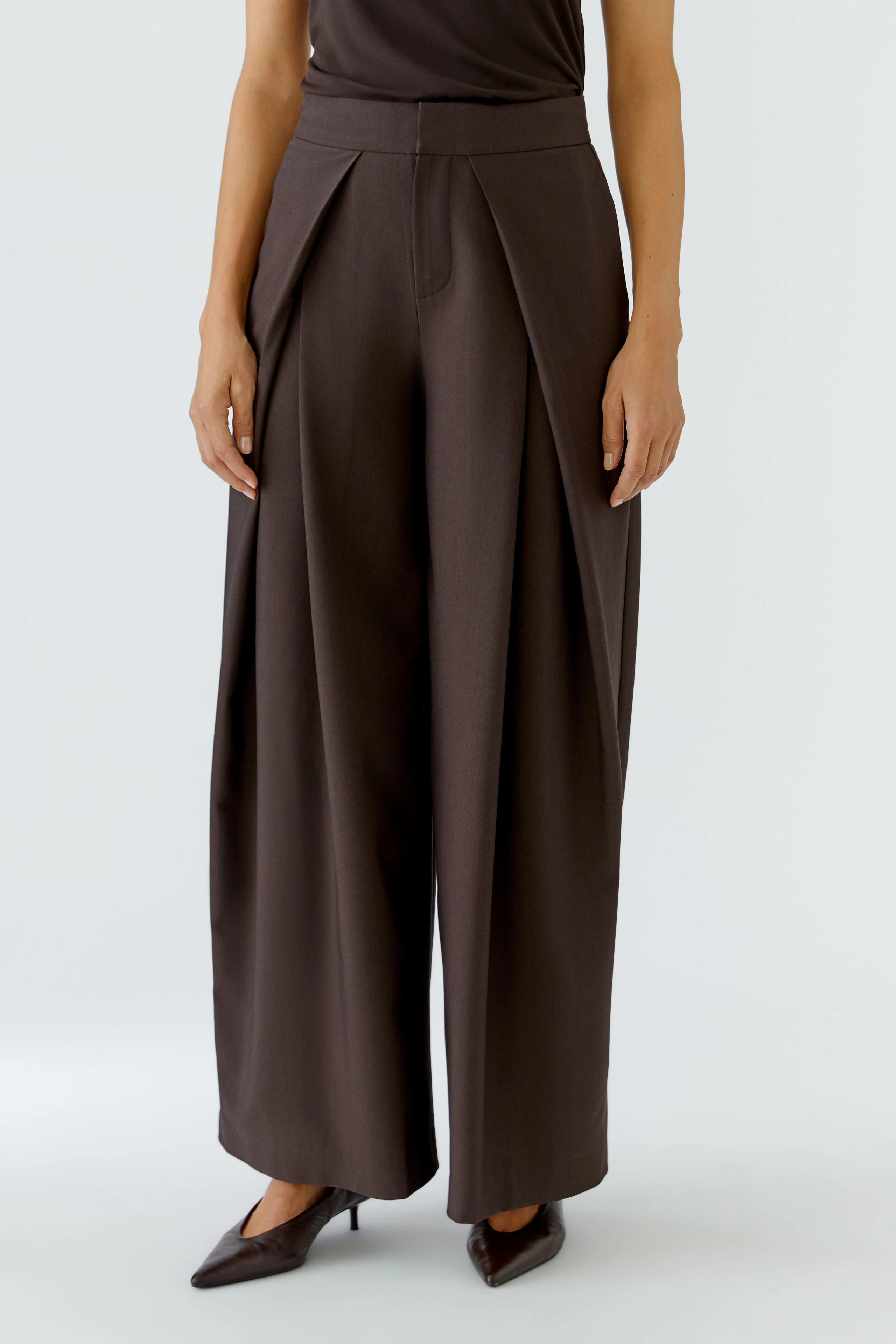Woman in brown pleated trousers, standing confidently. Wide-leg design with a high waist.