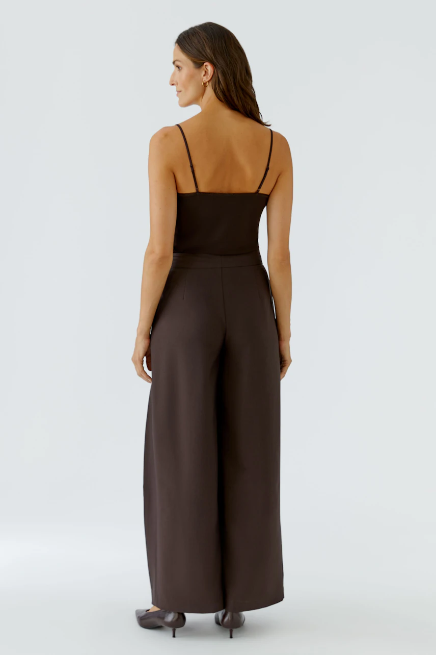 Woman in brown pleated trousers, sleeveless top, and flats, showcasing a relaxed, modern style.