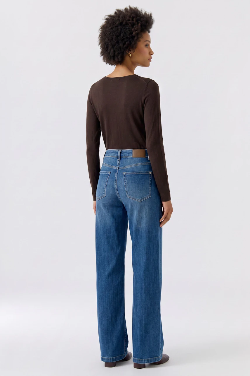 Frau im braunen Langarmshirt und blauer Jeans, Rückansicht. Lässiger Look für den Alltag.