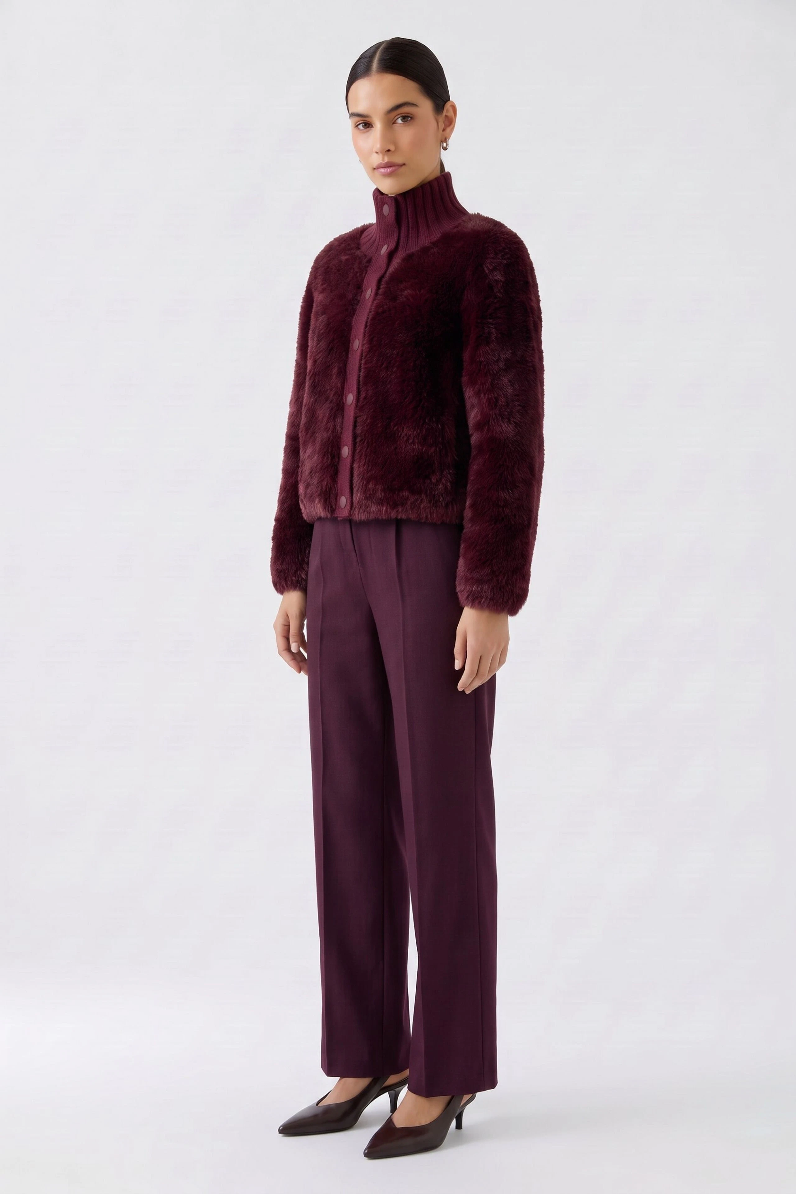 Frau in weinroter Strickjacke: Stehkragen, Knopfleiste, kombiniert mit passender Hose und Pumps.