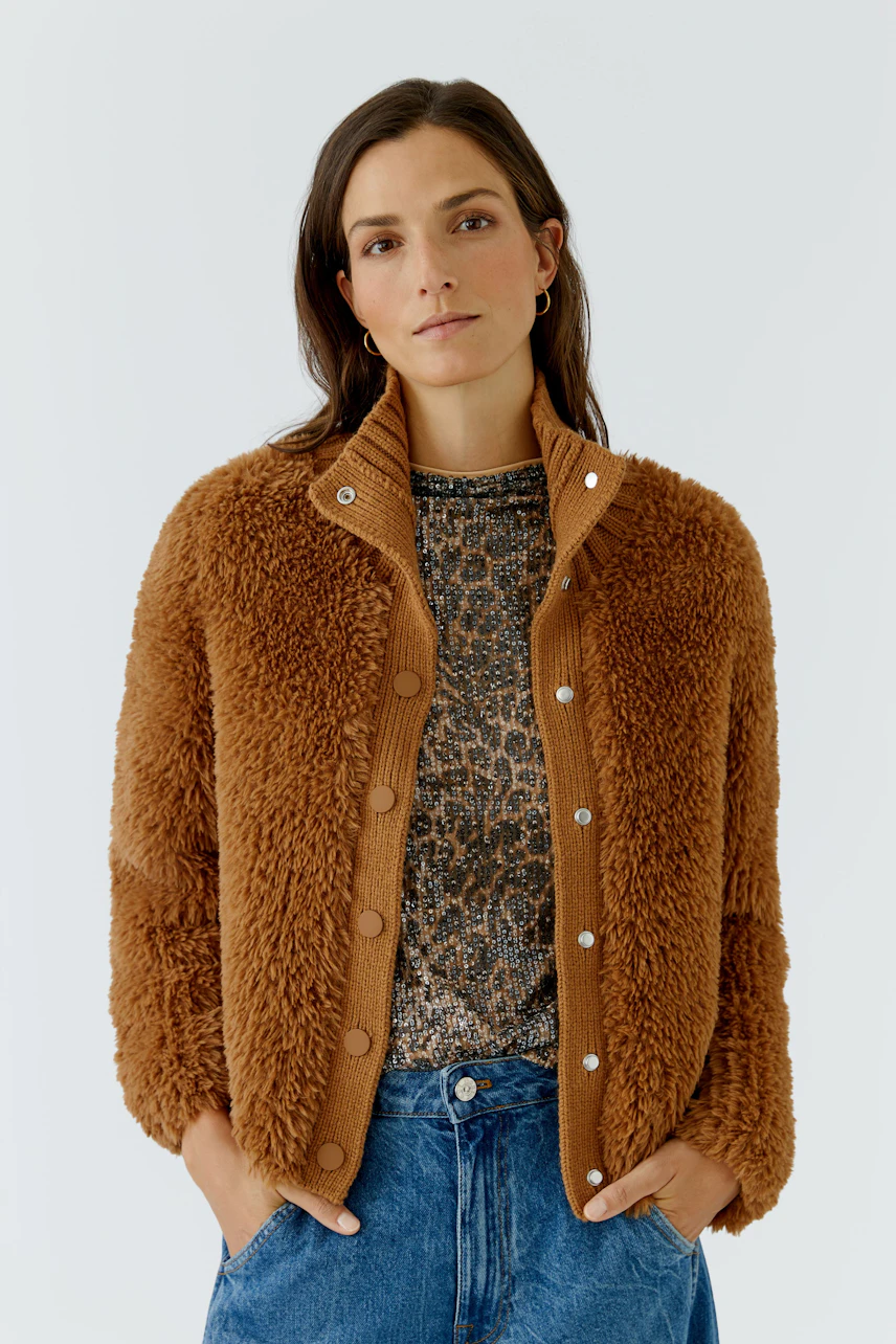 Frau in brauner Strickjacke mit Knöpfen, kombiniert mit Leoparden-Top und blauer Jeans, schaut direkt.