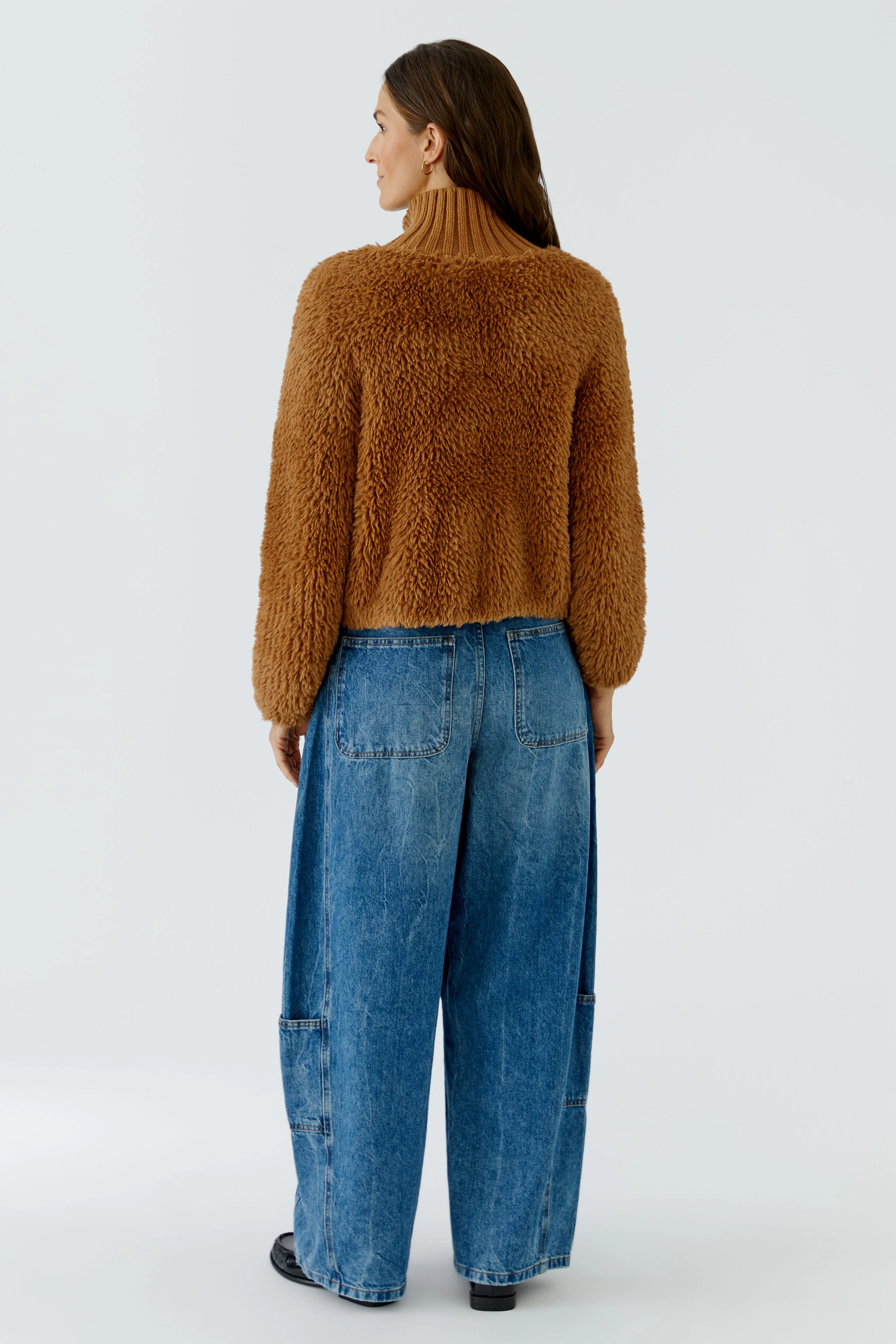 Woman in cozy brown cardigan, wide blue jeans, and black shoes, viewed from the back.
