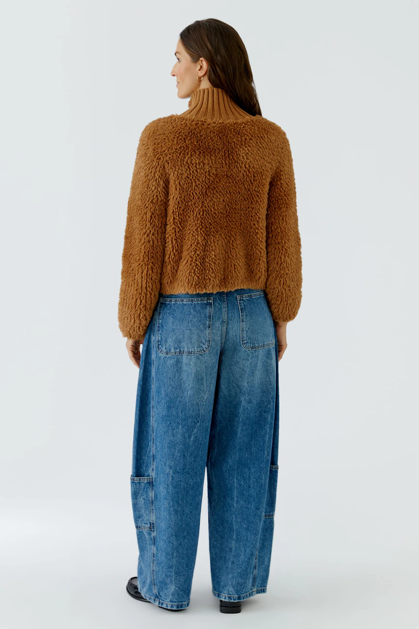 Frau in brauner Strickjacke und blauer Jeans, Rückansicht. Lässiger Look für kühle Tage.
