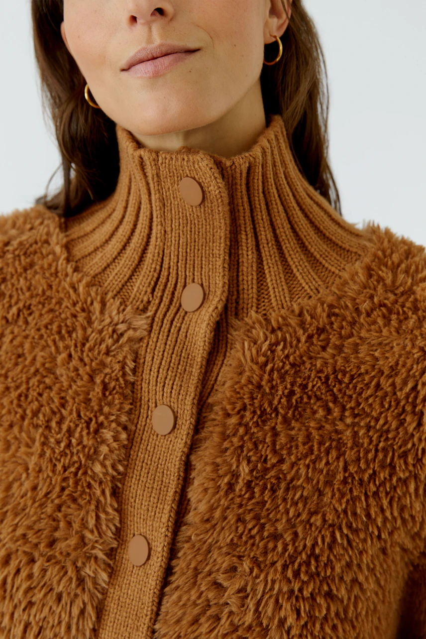 Frau in brauner Strickjacke mit Knöpfen und hohem Kragen, lässiger Look.