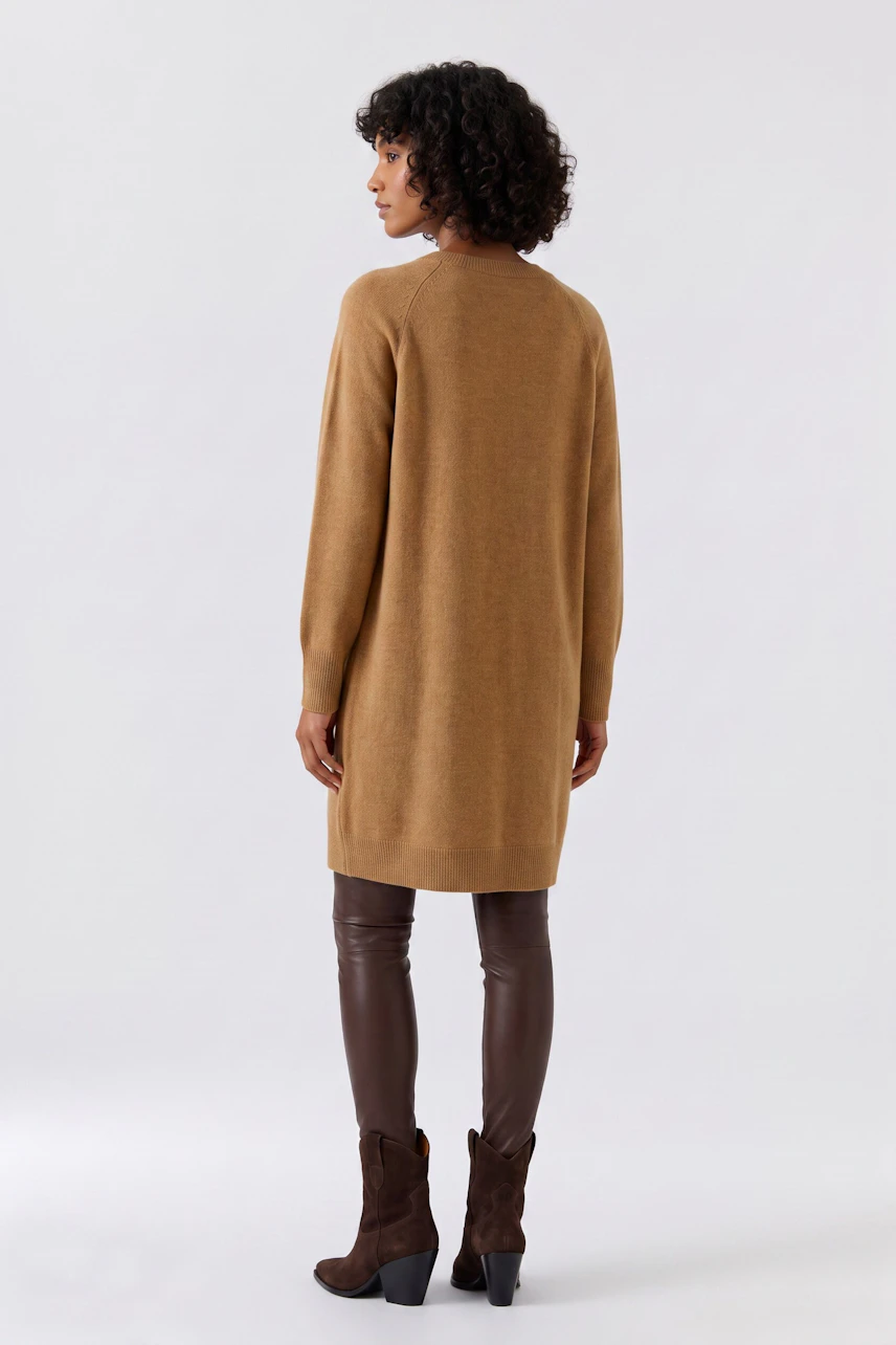 Woman in a brown knit dress, paired with brown leather leggings and boots, standing confidently.