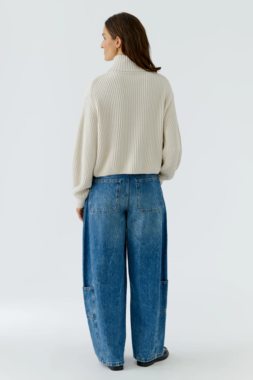 Frau im cremefarbenen Pullover und blauer Jeans, Rückansicht. Lässiger Look für den Alltag.
