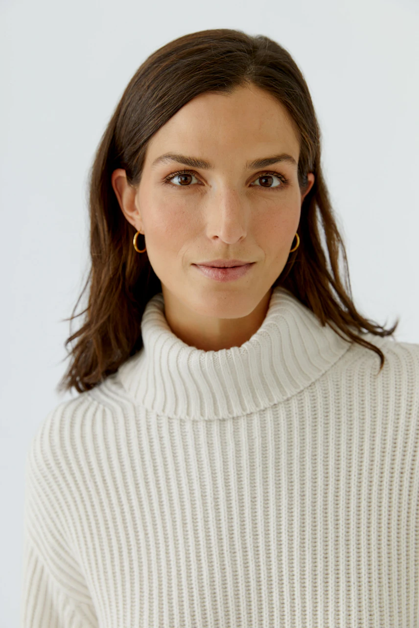 Frau im weißen Rollkragenpullover aus Strick, schlicht und modern, mit dezentem Look.