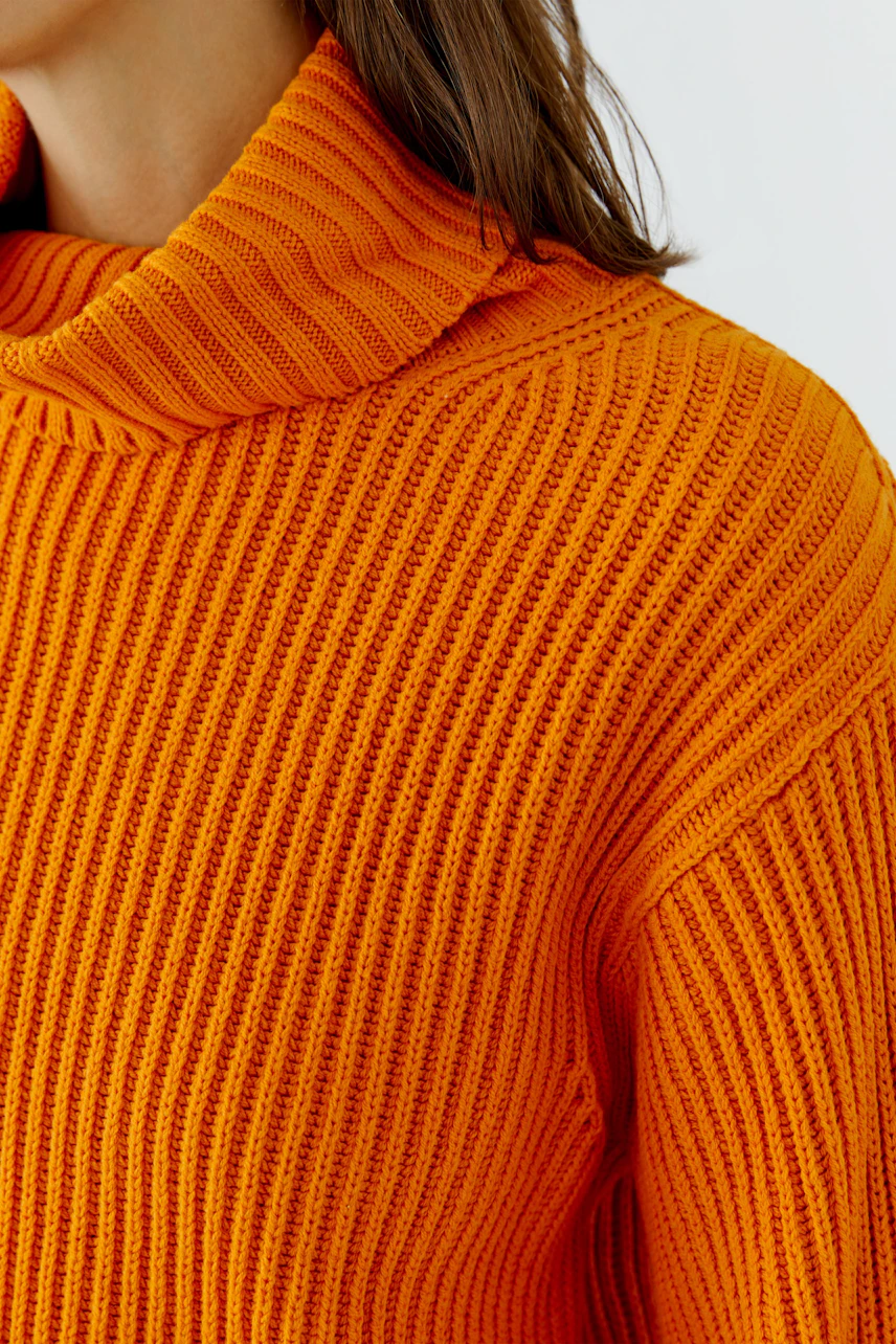 Frau im orangefarbenen Pullover mit Rollkragen, grob gestrickt, zeigt modernen Stil.