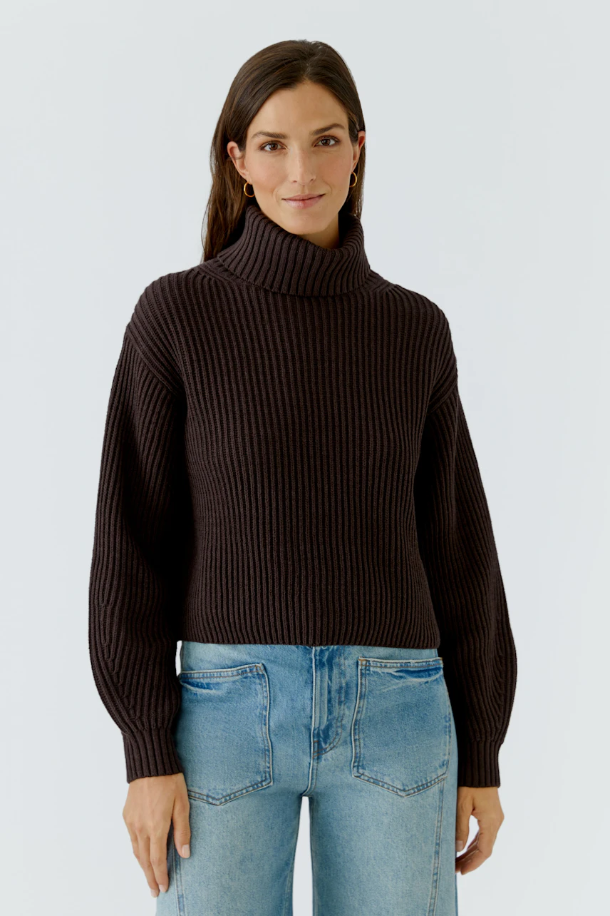 Casual women's pullover: Woman in a dark ribbed pullover with a turtleneck and relaxed fit, paired with jeans.
