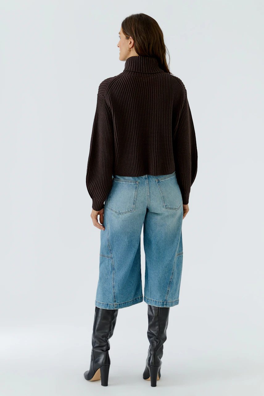 Casual pullover: Woman in a dark ribbed pullover, blue jeans, and black boots, viewed from the back.