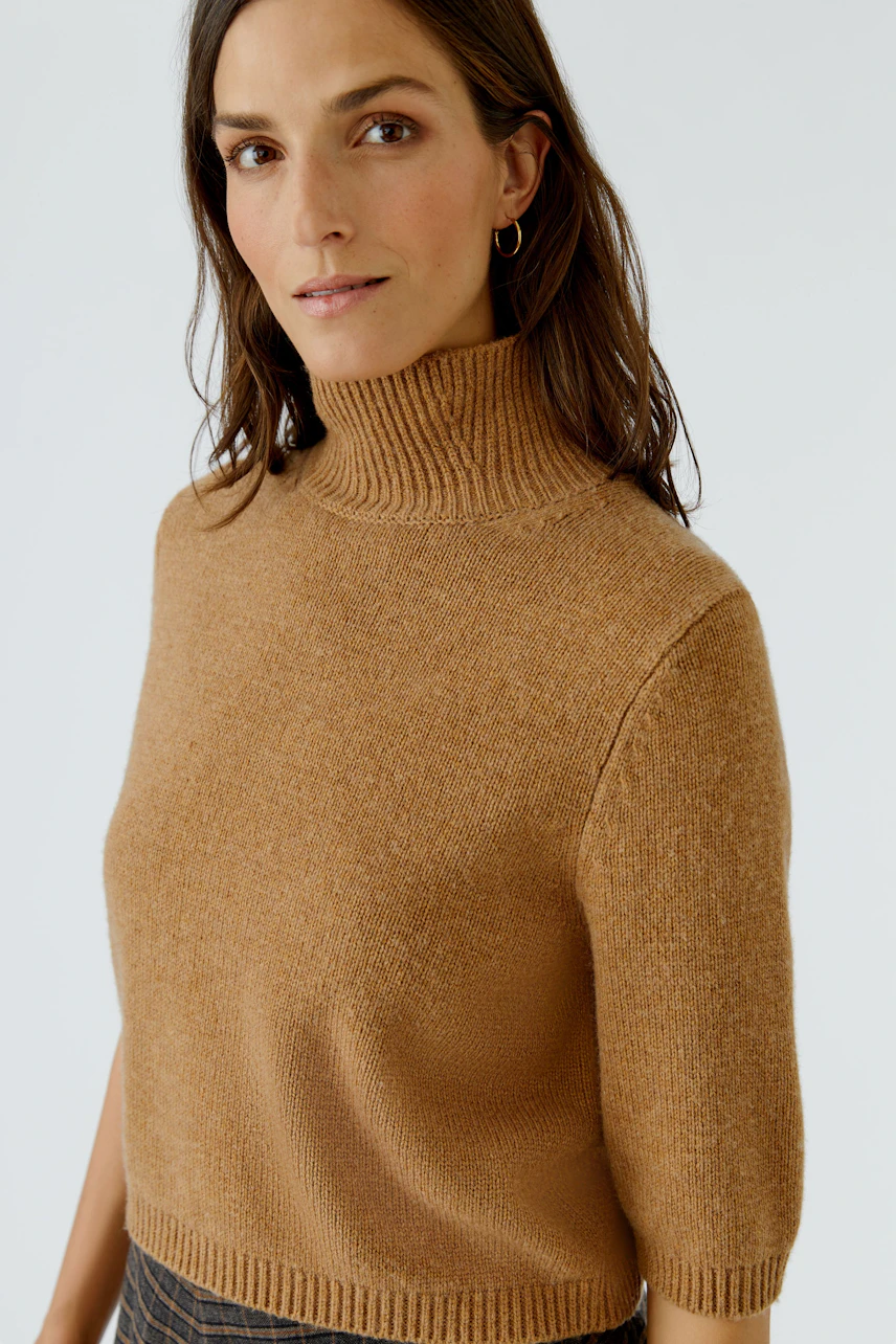 Frau im braunen Pullover mit halblangen Ärmeln und Rollkragen, lässiger Look.