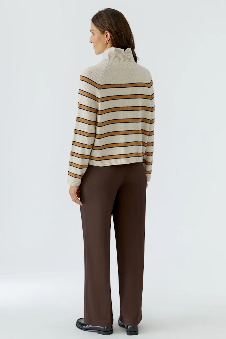 Gestreifter Damen-Pullover: Frau im beige-braunen Pullover mit Rollkragen und brauner Hose von hinten.